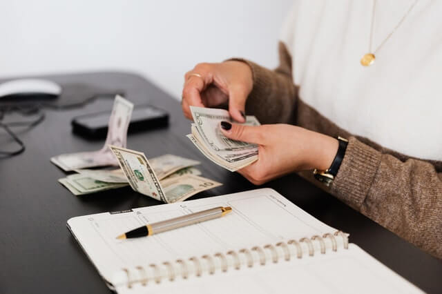 Nosotros crop payroll clerk counting money while sitting at table