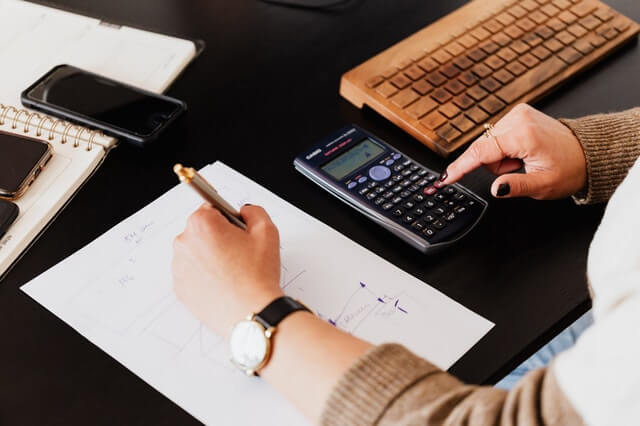 Proyectos crop woman using calculator and taking notes on paper